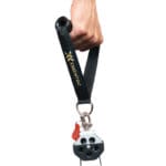 A hand holds the Exxentric kGrip pulley device featuring a metallic body, three circular cutouts on the wheel, a red tag, and a black strap with EXXENTRIC labeled. The handle of the strap is firmly gripped.