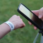 Someone holds a smartphone toward a wrist wearing a Dashr Barcode Wrist Band, likely scanning it against the grassy outdoor backdrop.