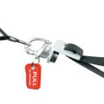 Close-up of the Exxentric Single Turnbuckle: a metal hook clasp on a black strap with a red PULL to release tag, designed for quick detachment.