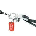 Close-up of the Exxentric Single Turnbuckle: a metal hook clasp on a black strap with a red PULL to release tag, designed for quick detachment.