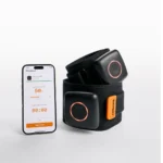A smartphone with a workout app stands beside AirBands 2.0, a black wearable fitness device featuring orange-accented adjustable straps and square modules.