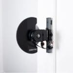 A black Exxentric kPulley GO, designed for resistance training, is mounted on a white wall. It has a compact design with a circular flywheel and electronic components attached.