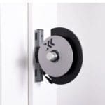 A wall-mounted retractable belt barrier echoes the sleek design of Exxentrics kPulley GO, featuring a silver circular mechanism holding a black belt. It extends smoothly to block or direct passage, blending seamlessly into the minimalistic white wall.