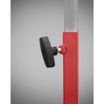 A close-up of the PowerMax Vertical Jump Trainer showcases its red adjustable metal stand with a black plastic handle attached to a screw mechanism for height adjustment against a neutral gray background.