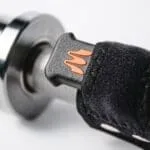 Close-up of a motorcycle handlebar grip with Enode Replacement Barbell Strap in black and orange attached to the throttle control. The grip has a textured surface, and the strap uses Velcro for secure fastening.