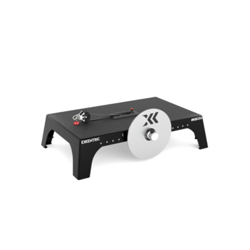 An exercise machine featuring a flat black base with a silver resistance disc and a handle attached to a cord. The device is labeled Exxentric kBox4 on the side, designed for strength training.
