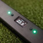 A close-up of an OVR Performance Velocity VBT (Copy) golf putting aid on artificial turf shows a 23.9-inch measurement and two green indicator lights beside the screen.