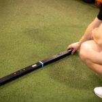 A person kneels on artificial turf beside a long, black OVR Performance Jump device, featuring small indicator lights and buttons on its surface.