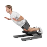 A man in athletic wear performs a back extension on a black VALD NordBoard, leaning forward with arms extended back and legs secured under padded supports.