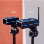 Two OVR Performance Sprint Starter Kit sensors with blue stripes are mounted on tripods on a track, one with an antenna visible. The blurred background includes red and gray track lanes.
