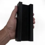 A hand holds the Skyhook Modular Plyo Box, a black, U-shaped plastic object with flat sides and a hollow center, against a white background.