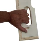 A hand holds the Skyhook Modular Plyo Box, featuring a rectangular piece of plywood with a rounded cutout handle, visible edges, and a smooth, light-colored finish.