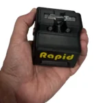 A hand holds a Rapid Remote Release, a black plastic tool with a yellow "Rapid" label, featuring a metal component and screws on top.