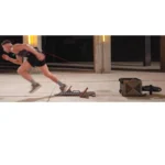 A man in athletic gear sprints from starting blocks indoors, attached to a TAPEX resistance trainer by a red cord. The space features concrete floors and columns in the background.