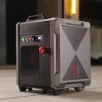 A rugged gray and black TAPEX portable power unit with a handle, control buttons, and digital display is placed on a concrete floor in an industrial environment.