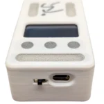 A close-up of the Dashr Vert, a small white electronic device featuring a screen, three round gray buttons, a switch, and a micro USB port on its front panel.