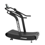 The TRUEFORM Trainer is a black, curved manual treadmill with handlebars and a digital display, featuring the TRUEFORM logo on its upright frame, designed for running or walking workouts.