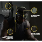 In a dimly lit gym, someone wears the Iron Neck Alpha Harness, which includes two side straps for a snug fit, ultra-durable stitching, a stainless steel D-ring with carabiner connection, and a nylon tether for smoother lifts.