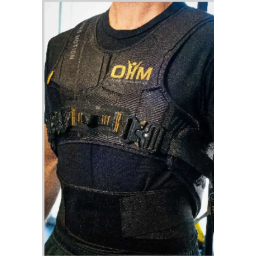 A person wearing the OHM Power Harness, a black padded vest featuring the yellow OHM logo on the chest, with adjustable straps and front buckles.