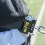 Close-up of a person on a grassy sports field with a white line, wearing a belt with the Rapid Release device attached to a carabiner.