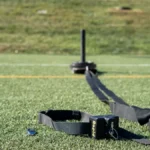 The Rapid Release weighted sled, featuring a black strap and harness, rests on artificial turf with a grassy field and yellow line behind it—ideal for athletic training and conditioning.