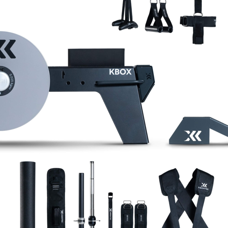 The kBox Ultimate System flywheel training device is shown with black and gray fitness accessories—straps, bars, and attachments—arranged around it on a white background.